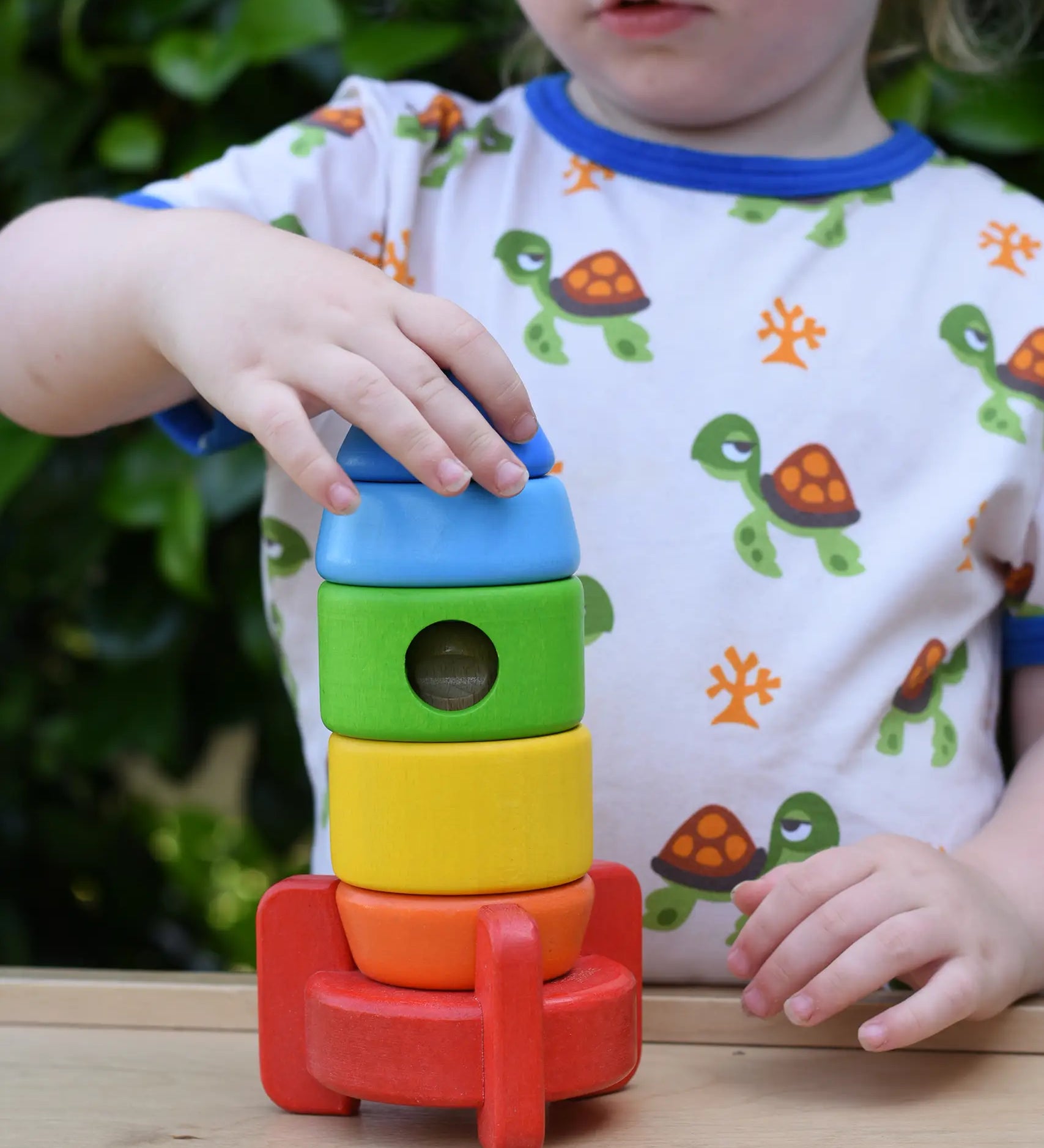 Child placing the top pieces on the Bajo stacking rocket wooden toy.