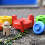 Bajo stacking rocket wooden toy red base piece placed on a stone wall wit the pieces besides it.