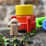 Natural wood astronaut figures placed in front of the Bajo stacking rocket wooden toy on a stone wall.
