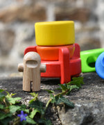 Natural wood astronaut figures placed in front of the Bajo stacking rocket wooden toy on a stone wall.
