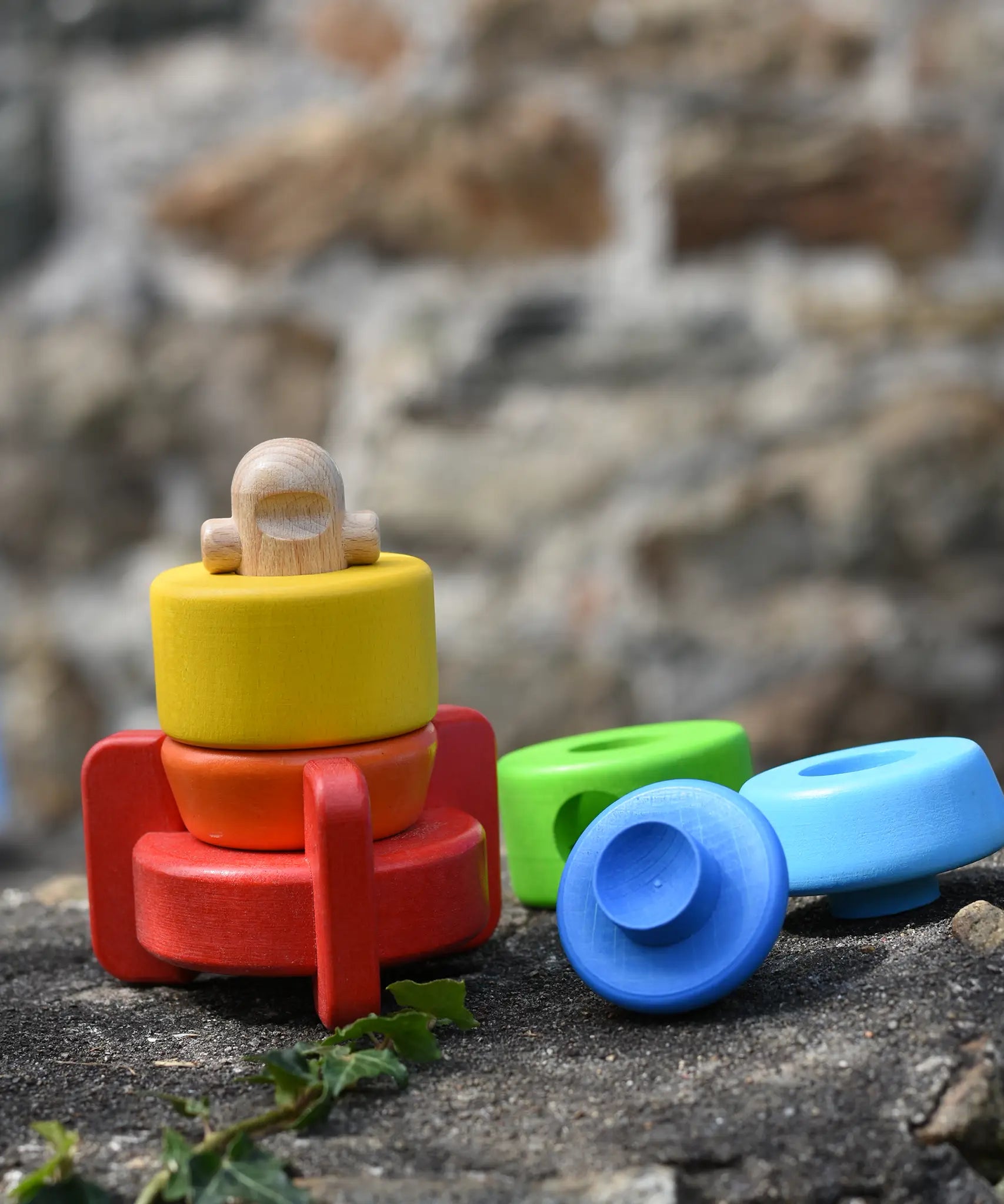 Bajo stacking rocket wooden toy placed on a stone wall, the top three pieces have been placed besides the base piece.
