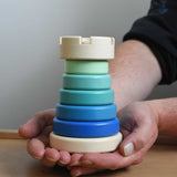 A close up of the blue coloured Bajo wooden rook stacking tower toy in a adult's hand. These heirloom quality toys by Bajo are part of a wide range of wooden toys available here at Babipur.