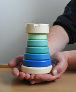 A close up of the blue coloured Bajo wooden rook stacking tower toy in a adult's hand. These heirloom quality toys by Bajo are part of a wide range of wooden toys available here at Babipur.