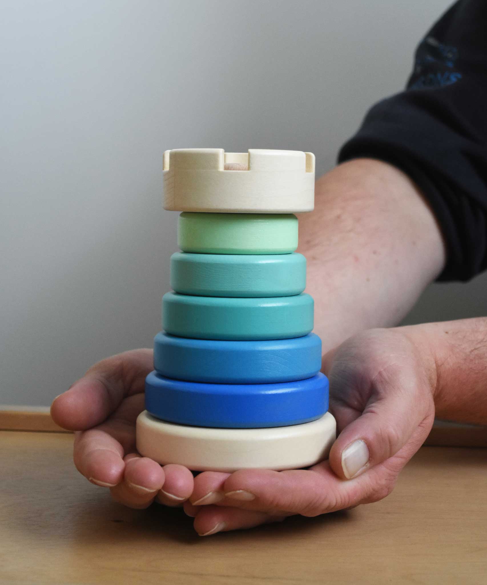 A close up of the blue coloured Bajo wooden rook stacking tower toy in a adult's hand. These heirloom quality toys by Bajo are part of a wide range of wooden toys available here at Babipur.