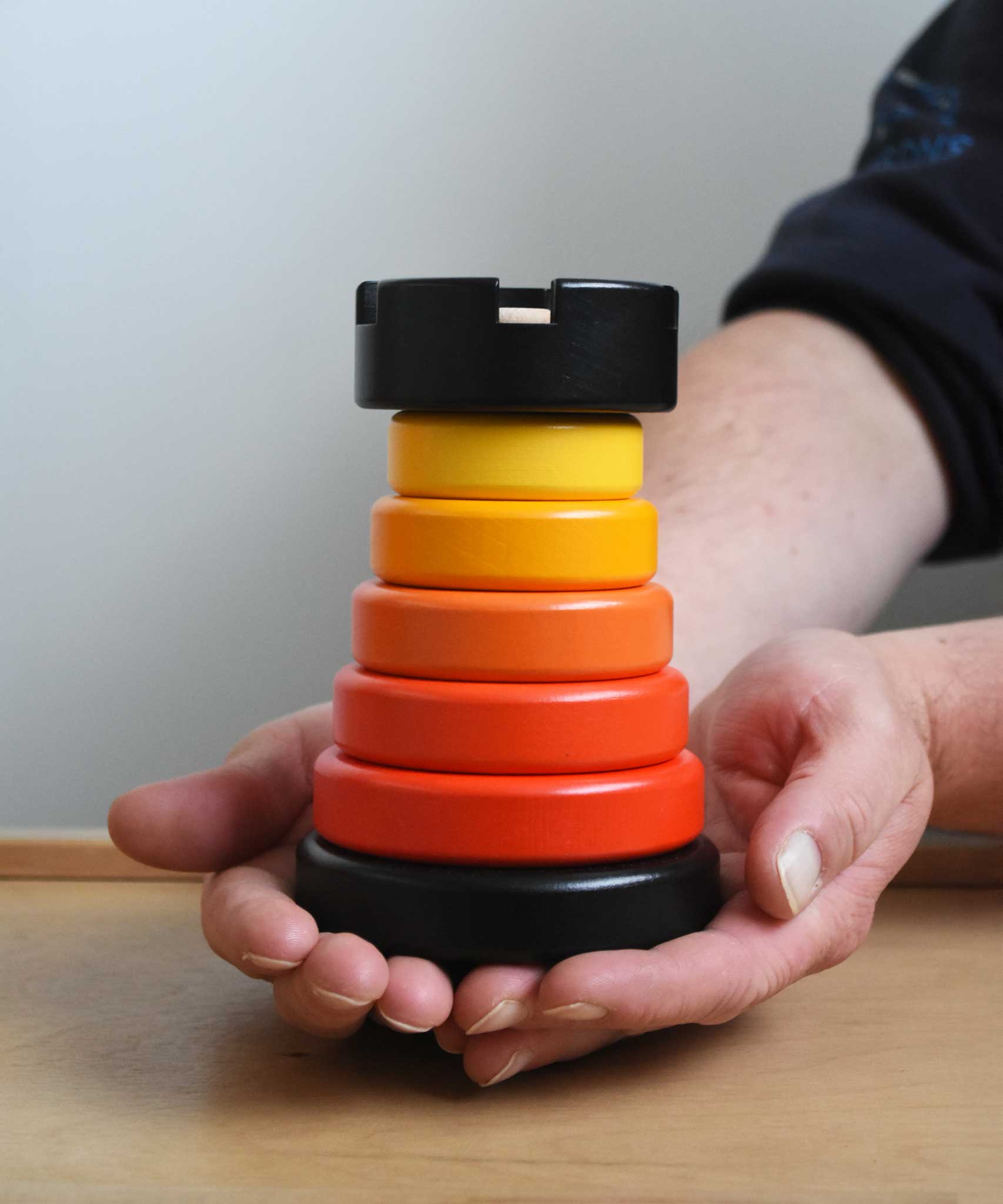 A close up of the red coloured Bajo wooden rook stacking tower toy in a adult's hand. These heirloom quality toys by Bajo are part of a wide range of wooden toys available here at Babipur.