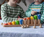 Bajo rope abacus toy with 10 pegs each with wooden rings from 1 to 10. Children in the background.