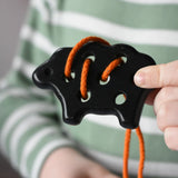 Bajo wooden lacing black lamb toy with orange lace in a child's hand.
