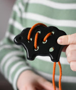 Bajo wooden lacing black lamb toy with orange lace in a child's hand.