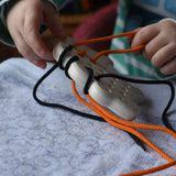 Bajo wooden lacing sheep with orange and black threads. Child pulling orange lace out.