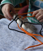 Bajo wooden lacing sheep with orange and black threads. Child pulling orange lace out.