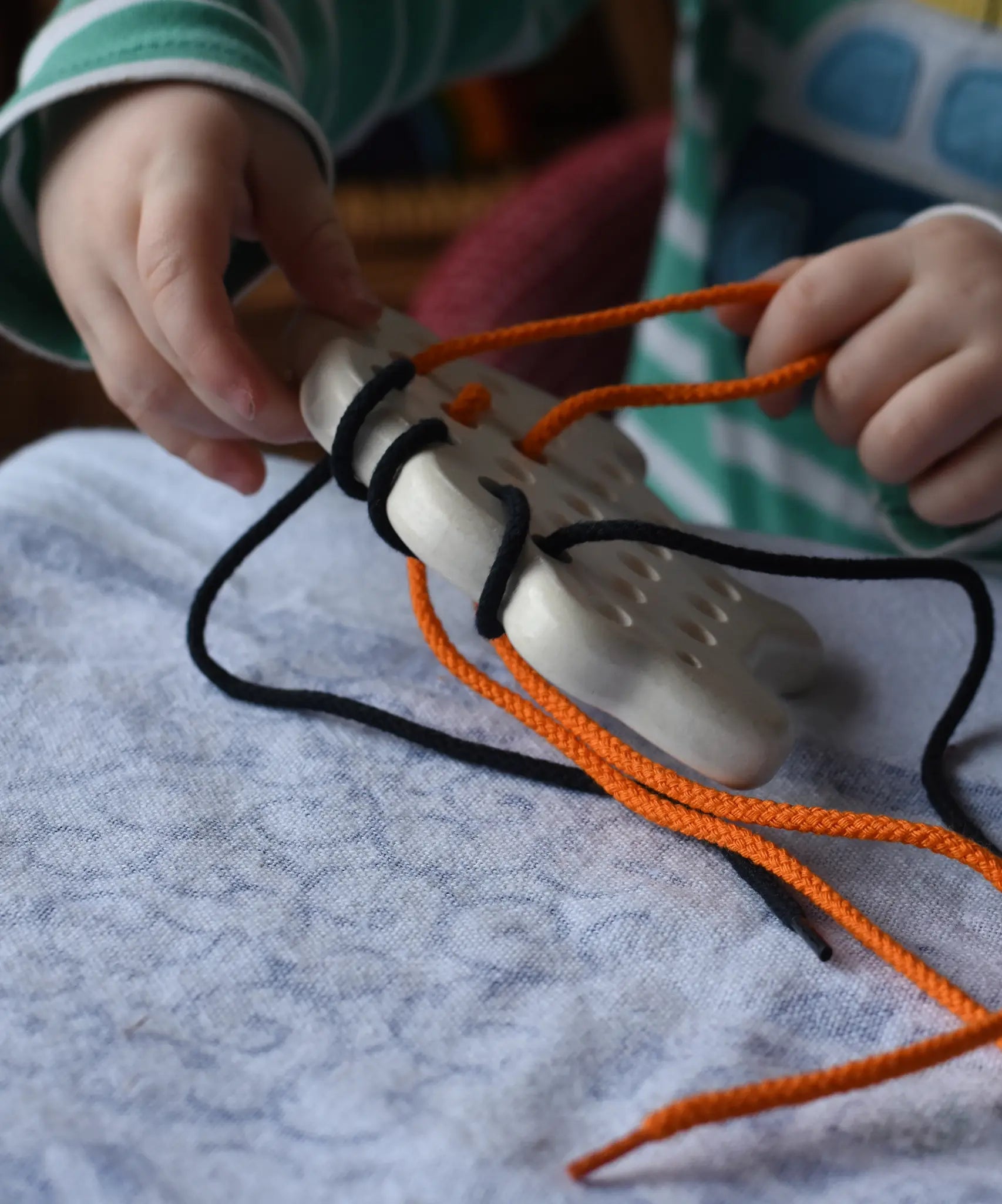 Bajo wooden lacing sheep with orange and black threads. Child pulling orange lace out.
