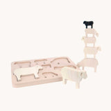 Bajo Sheep Puzzle. A wooden frame with 7 sheep shaped figures. Some of the figures are placed in the frame with others placed in a stack by the side of the frame.