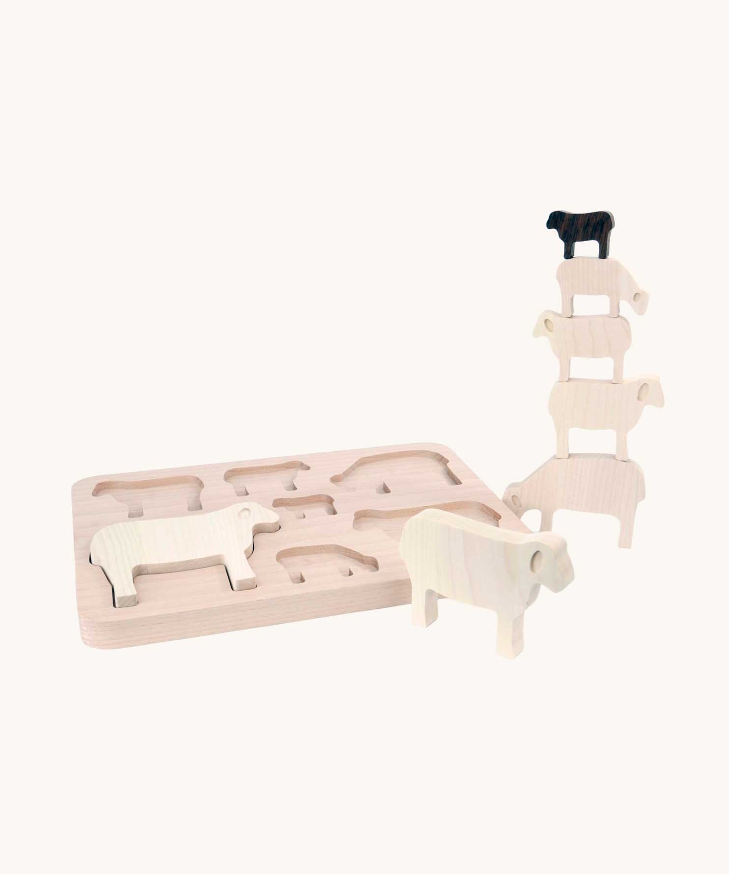 Bajo Sheep Puzzle. A wooden frame with 7 sheep shaped figures. Some of the figures are placed in the frame with others placed in a stack by the side of the frame.