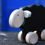Close up of the face on the Bajo black sheep push along wooden toy on wheels placed on a stone wall outdoors.