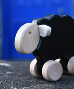 Close up of the face on the Bajo black sheep push along wooden toy on wheels placed on a stone wall outdoors.