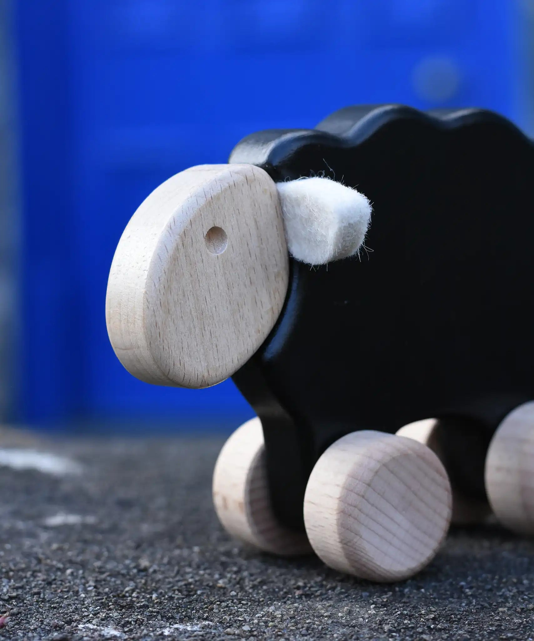 Close up of the face on the Bajo black sheep push along wooden toy on wheels placed on a stone wall outdoors.