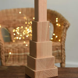 The blocks from the Bajo Square Pyramid Sensory Wooden Stacking Toy shown staked up on a small wooden table.  The set contains 5 wooden square and rectangular shaped blocks with a different coloured bases. Each blocks make a different sound when shaken. These heirloom quality toys by Bajo are part of a wide range of wooden toys available here at Babipur. 