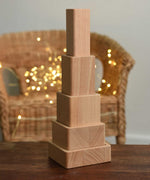 The blocks from the Bajo Square Pyramid Sensory Wooden Stacking Toy shown staked up on a small wooden table.  The set contains 5 wooden square and rectangular shaped blocks with a different coloured bases. Each blocks make a different sound when shaken. These heirloom quality toys by Bajo are part of a wide range of wooden toys available here at Babipur. 