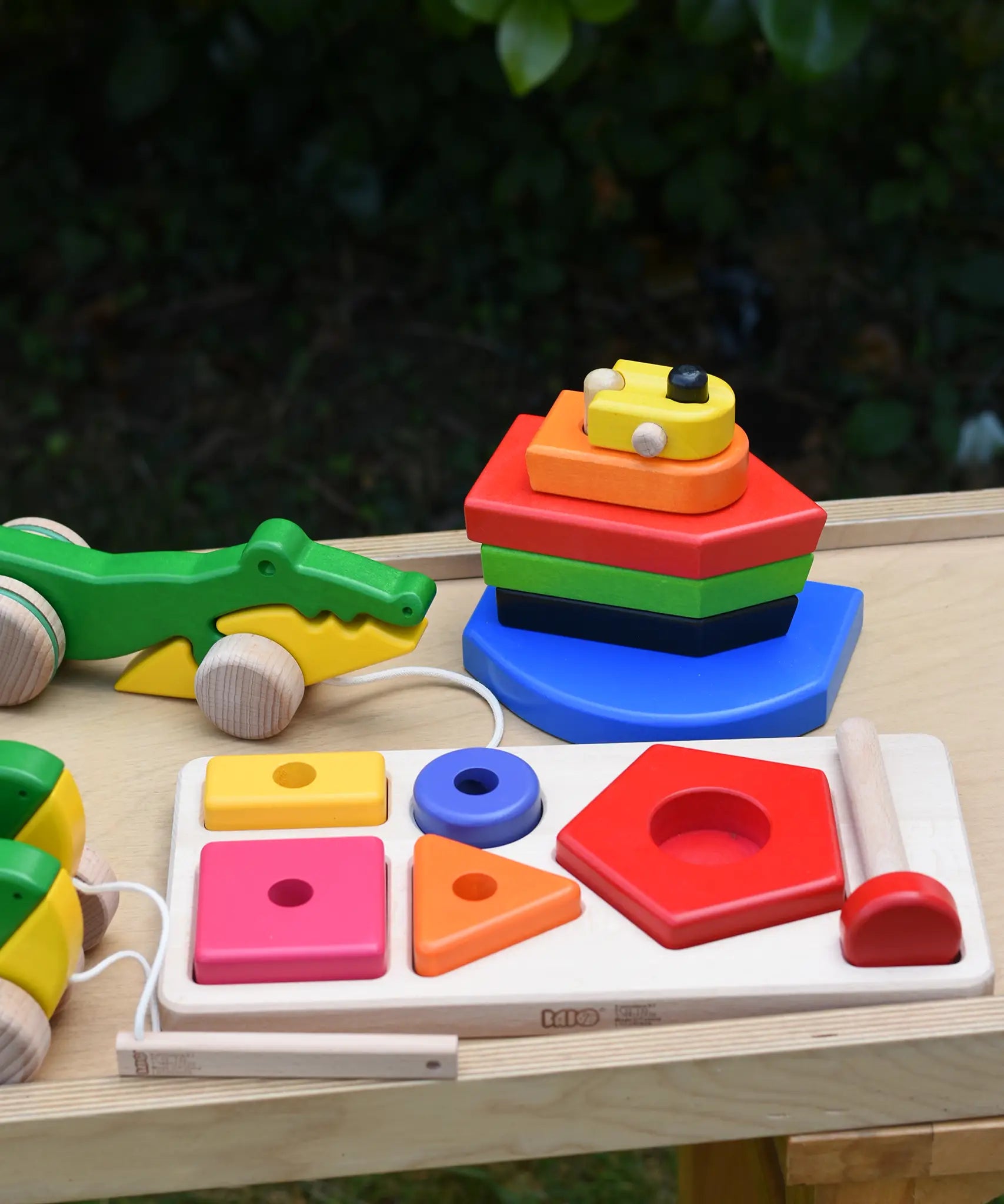 Bajo wooden toys placed on a wooden surface, nemo boat stacker toy, pyramid sorting board and crocodile pull along.