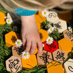 Close up of a child's hand playing with the Bajo wooden hive block toys next to some white flowers