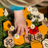 Close up of a child's hand playing with the Bajo wooden hive block toys next to some white flowers