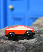 Bajo red ToBe Poly car wooden toy on a stone wall.
