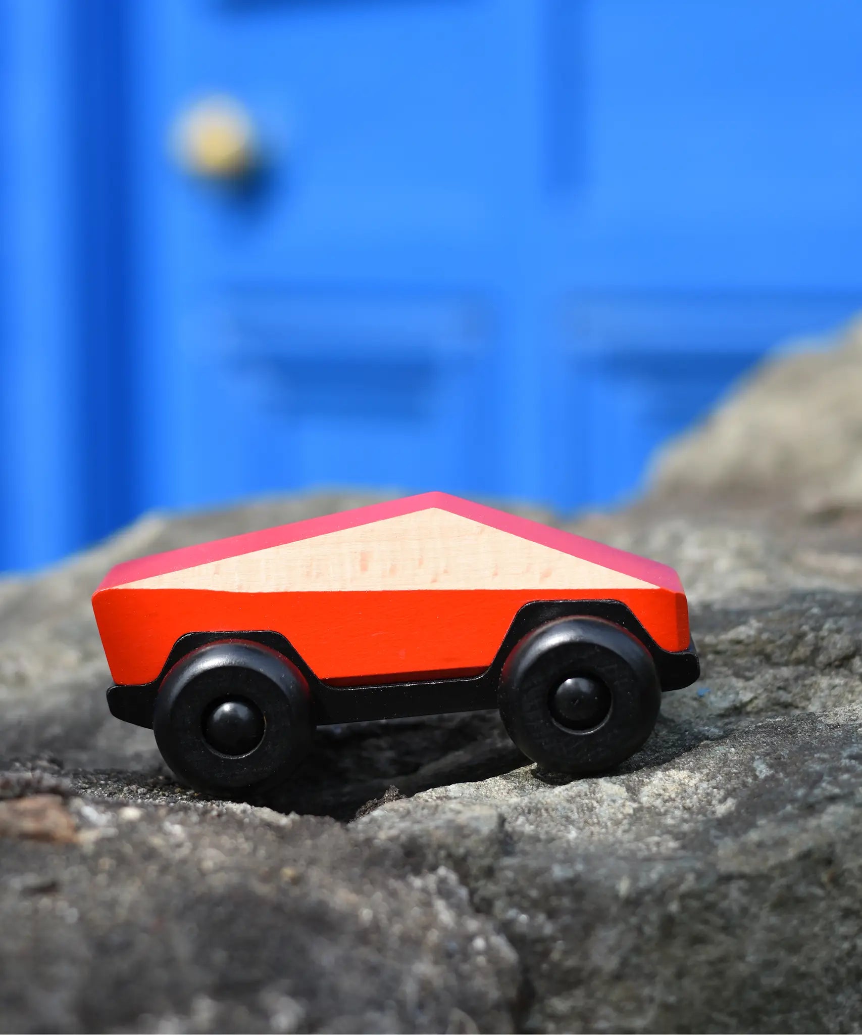 Bajo red ToBe Poly car wooden toy on a stone wall.