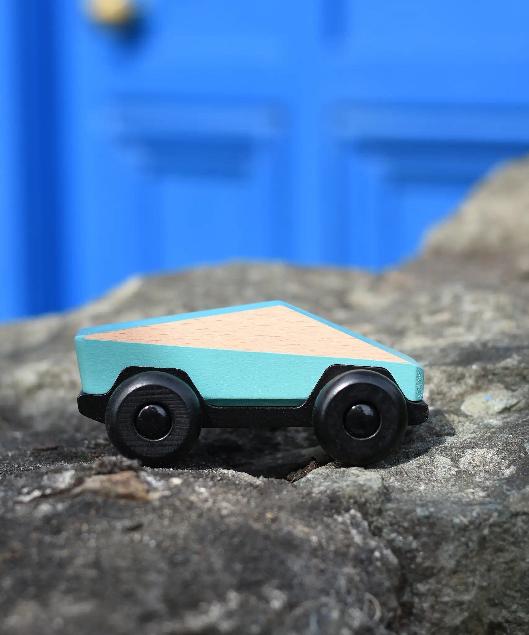 Bajo blue ToBe Poly car wooden toy on a stone wall.