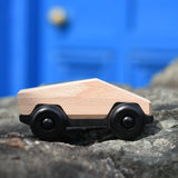 Bajo natural ToBe Poly car wooden toy on a stone wall.