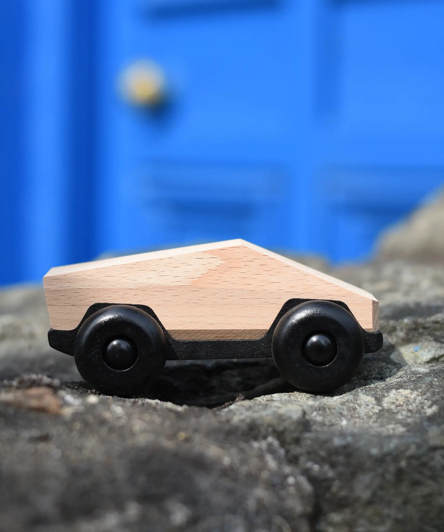 Bajo natural ToBe Poly car wooden toy on a stone wall.