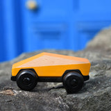 Bajo yellow ToBe Poly car wooden toy on a stone wall.