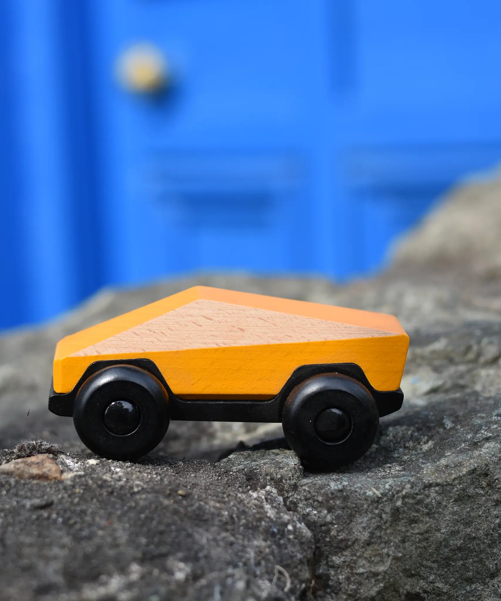 Bajo yellow ToBe Poly car wooden toy on a stone wall.