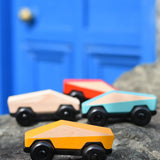 Bajo yellow ToBe Poly car wooden toy on a stone wall with other colours in the ebackground.