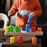 A child playing with the Bajo Balance Scale wooden toy. A wooden base with a curved base with coloured wooden blocks that sit on top. These heirloom quality toys by Bajo are part of a wide range of wooden toys available here at Babipur.