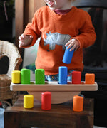 A child playing with the Bajo Balance Scale wooden toy. A wooden base with a curved base with coloured wooden blocks that sit on top. These heirloom quality toys by Bajo are part of a wide range of wooden toys available here at Babipur.