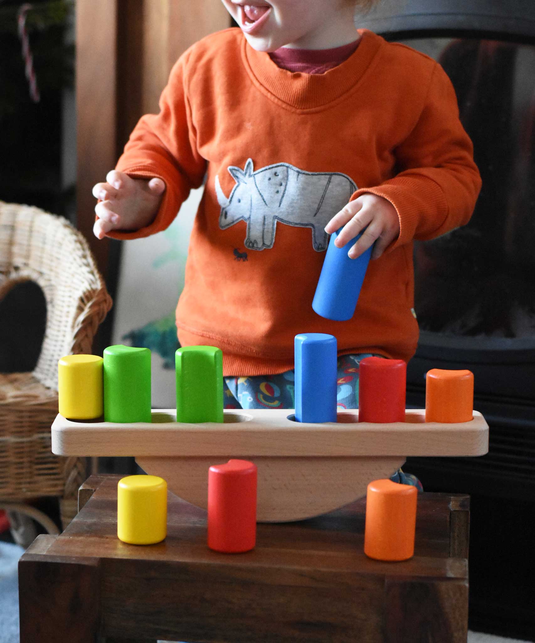 A child playing with the Bajo Balance Scale wooden toy. A wooden base with a curved base with coloured wooden blocks that sit on top. These heirloom quality toys by Bajo are part of a wide range of wooden toys available here at Babipur.