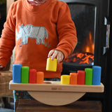 A child playing with the Bajo Balance Scale wooden toy. A wooden base with a curved base with coloured wooden blocks that sit on top. These heirloom quality toys by Bajo are part of a wide range of wooden toys available here at Babipur.