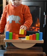 A child playing with the Bajo Balance Scale wooden toy. A wooden base with a curved base with coloured wooden blocks that sit on top. These heirloom quality toys by Bajo are part of a wide range of wooden toys available here at Babipur.