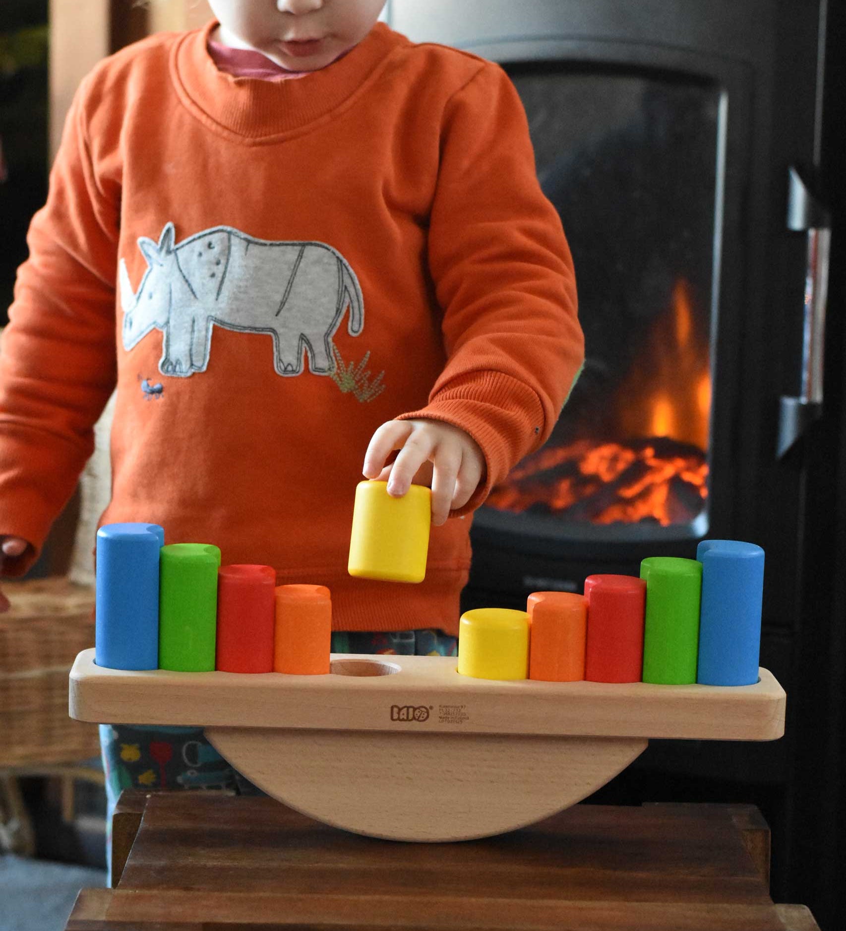 A child playing with the Bajo Balance Scale wooden toy. A wooden base with a curved base with coloured wooden blocks that sit on top. These heirloom quality toys by Bajo are part of a wide range of wooden toys available here at Babipur.