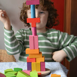 Bajo 43 wooden building blocks. Child stacking blocks on wooden lid of box into a high tower.