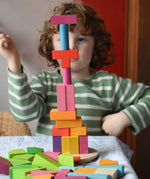 Bajo 43 wooden building blocks. Child stacking blocks on wooden lid of box into a high tower.