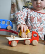 A child playing with a red coloured Bajo Auto Transporter. The wooden toy car transporter comes with two cars, one green and one blue. These heirloom quality toys by Bajo are part of a wide range of wooden toys available here at Babipur. 
