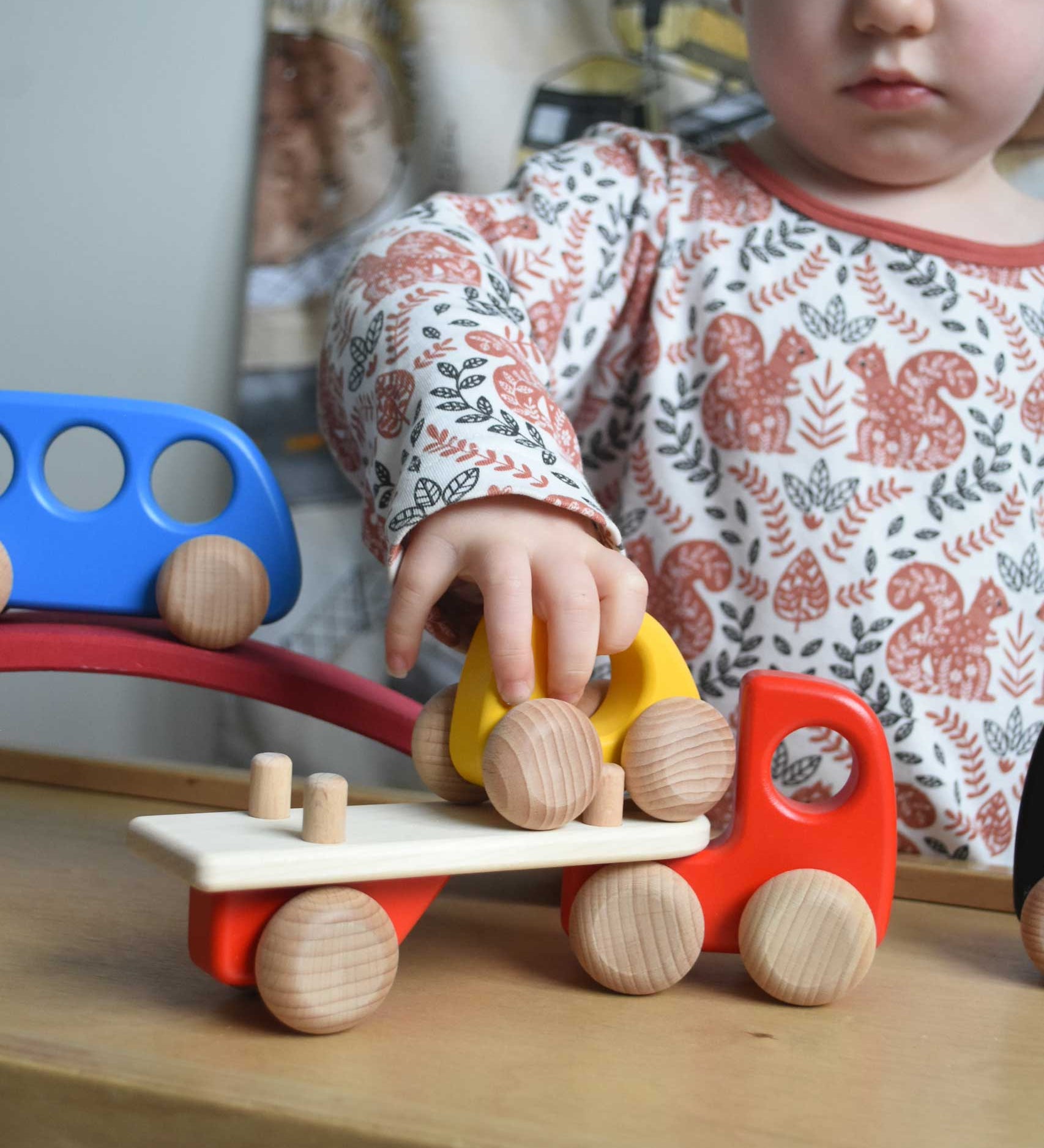 A child playing with a red coloured Bajo Auto Transporter. The wooden toy car transporter comes with two cars, one green and one blue. These heirloom quality toys by Bajo are part of a wide range of wooden toys available here at Babipur. 