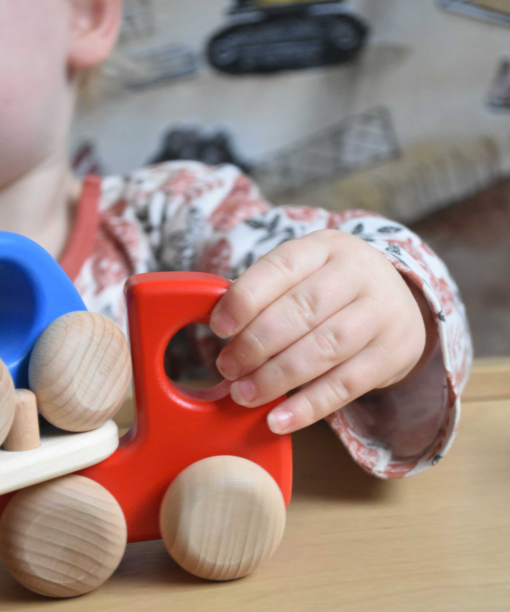 A close up of a child's hand holding on the front of the red coloured Bajo Auto Transporter. The wooden toy car transporter comes with two cars, one green and one blue. These heirloom quality toys by Bajo are part of a wide range of wooden toys available here at Babipur. 