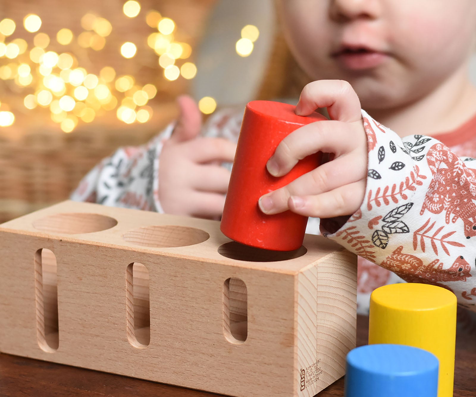 A child playing with the Bajo Deep And Shallow Sorter wooden toy placed on a small wooden table. These heirloom quality toys by Bajo are part of a wide range of wooden toys available here at Babipur. 