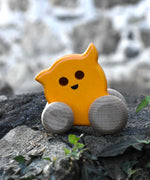A Bajo push along eye ghost wooden toy placed on a stone wall outdoors. Toe toy has a yellow painted body and natural wooden wheels. These heirloom quality toys by Bajo are part of a wide range of wooden toys available here at Babipur. 