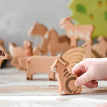 A child's hand holding the cat figure  from the Bajo farm animals set. Other animal figures can be seen in the background.