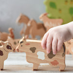 A child's hand holding the cow figure  from the Bajo farm animals set. Other animal figures can be seen in the background.