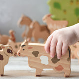 A child's hand holding the cow figure  from the Bajo farm animals set. Other animal figures can be seen in the background.