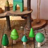 Bajo green forest tree set wooden toy figures placed on a wooden desk in the Babipur playroom with a Magic Wood adventure playground in the background.